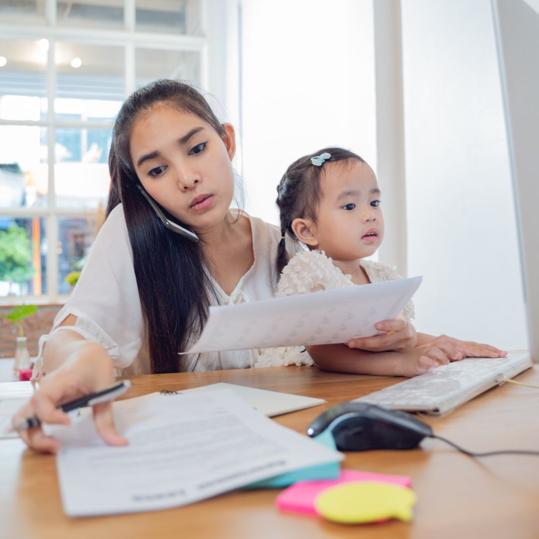 Mom on the phone and computer while holding daughter in her lap